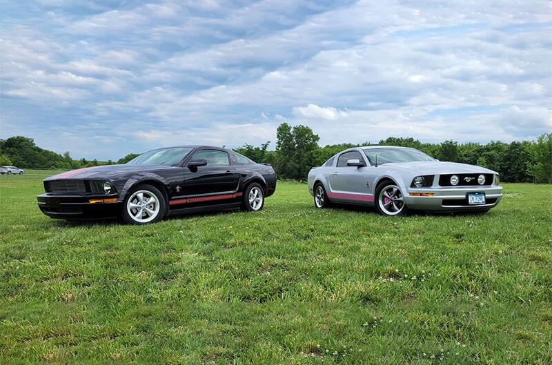 Two S197 Mustangs, one black one silver, parked on grass